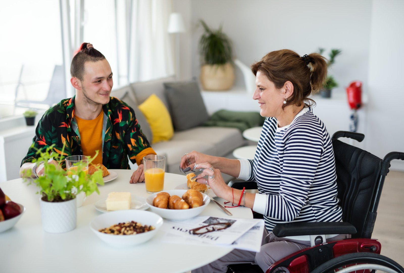 Woman in a wheelchair enjoying breakfast with a support worker – NDIS short term accommodation Sydney FAQs.
