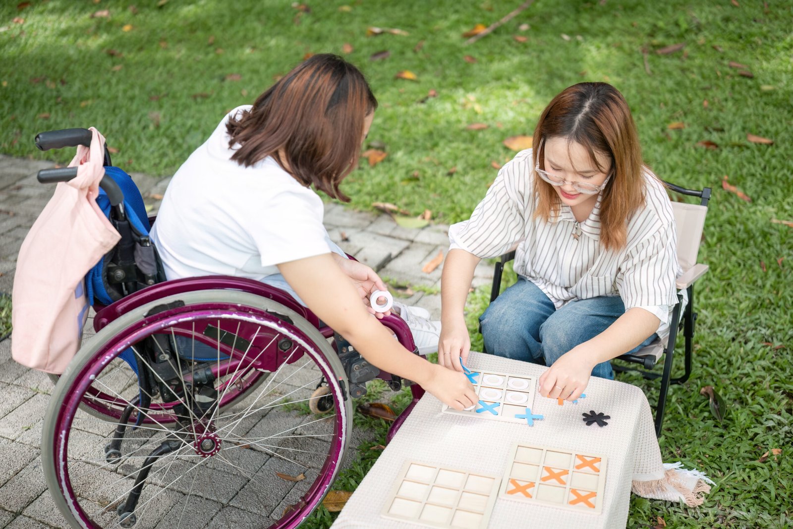Woman in a wheelchair and friend playing tic-tac-toe outdoors, enjoying NDIS Group & Centre-Based Activities at Improved Ability.